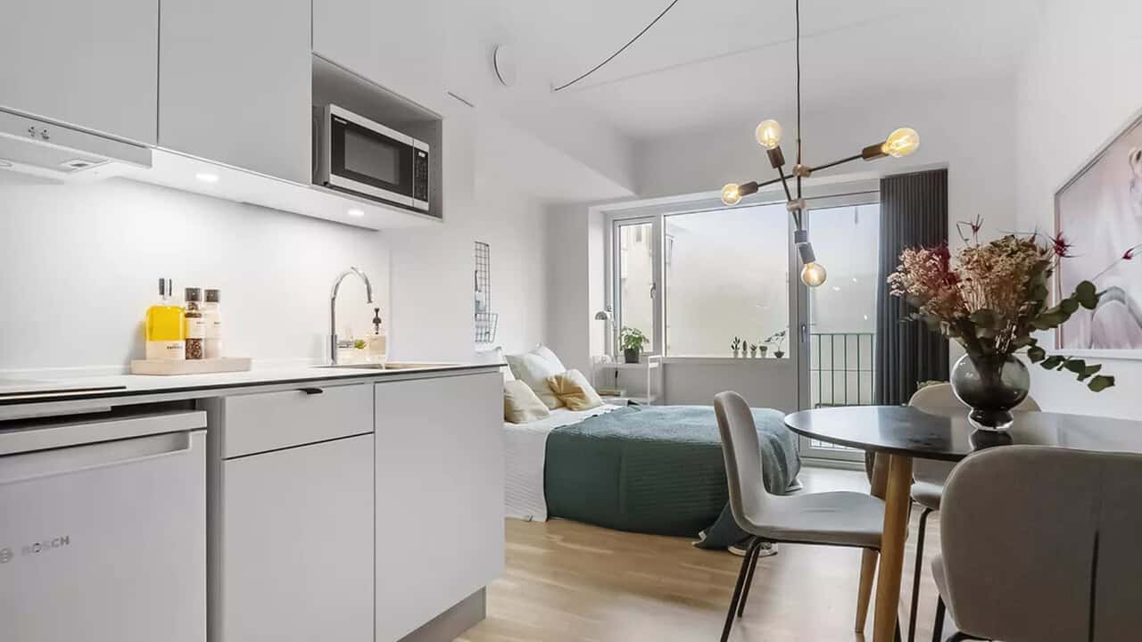 Liten modern uthyrningsdel med kök, säng, matbord och balkong i ett öppet rum.